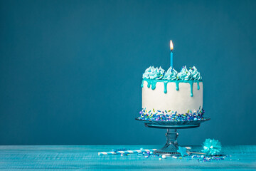 White birthday drip cake with teal ganache and lit candle over blue background - 580158286