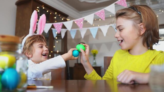 Easter Sunday Family holiday traditions. Two caucasian happy siblings kids with bunny ears fighting with multi-colored Easter painted eggs. Having fun together