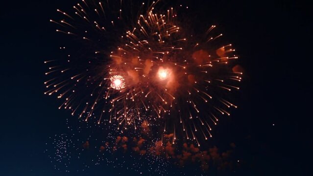 Beautiful big and small red fireworks explode against the background of the night sky, and sparks fly in all directions. High quality 4k footage