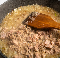 pan with food. wooden spoon, stirring the meat and vegetables.
