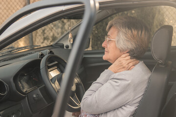 Senior woman having neck pain while driving a car. Old woman feeling bad about an injury,...