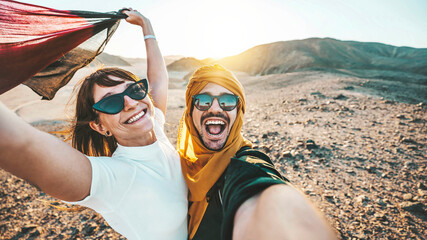 Happy couple of travelers taking selfie picture in rocky desert - Young man and woman having fun on summer vacation - Two friends enjoying summertime moment - Life style and travel concept.