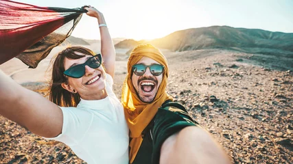 Fototapeten Happy couple of travelers taking selfie picture in rocky desert - Young man and woman having fun on summer vacation - Two friends enjoying summertime moment - Life style and travel concept. © Davide Angelini
