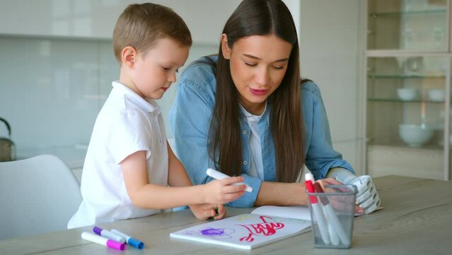 Mom with artificial hand prosthetic is painting in album with her son at home.