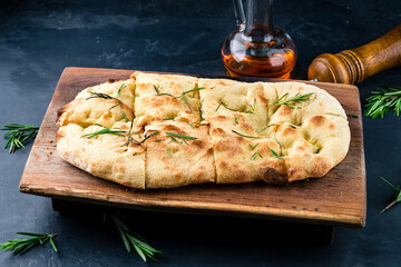Italian crispy pinsa with rosemary in wooden board.