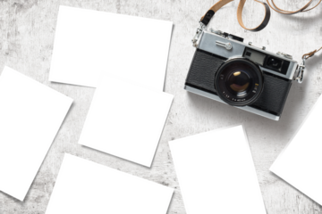 photo mockup / template with vintage analog camera and paper prints / images scattered on a white wooden table, top view / flat lay