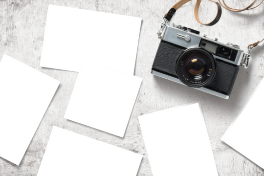 photo mockup / template with vintage analog camera and paper prints / images scattered on a white wooden table, top view / flat lay
