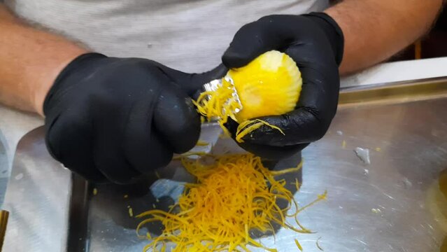 Male hands in black gloves remove the zest from a lemon with a special knife.
