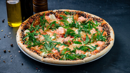 Italian pizza with salmon fish, cheese, tomato sauce, arugula and sesame seeds.