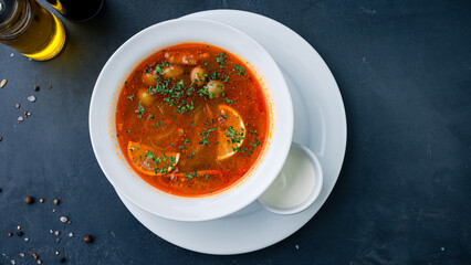 Solyanka soup with ham, meat, olives, tomatoes, sour cream lemon and greens.