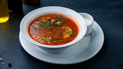 Fresh solyanka soup with ham, meat, olives, tomatoes, sour cream lemon and greens.