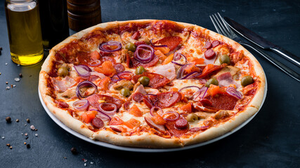 Italian pizza with ham, sausages, tomatoes, onion, olives, cheese and sauce.