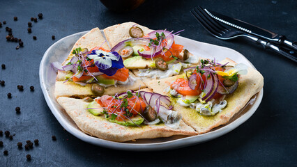 Fresh flatbread with salmon, avocado, onion and sauce on dark background.