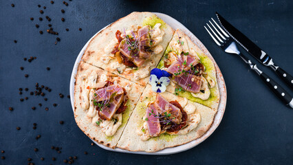 Flatbread with pieces of tuna, sun-dried tomatoes, microgreens and sauce.