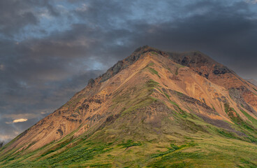 Denali Park, Alaska, USA - July 25, 2011: Focus on brown-green-black mountain peak against black-blue foggy sky. Green tundra at bottom