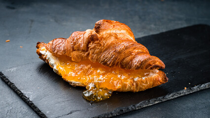 French breakfast fresh croissant with orange jam and cream cheese on black background.