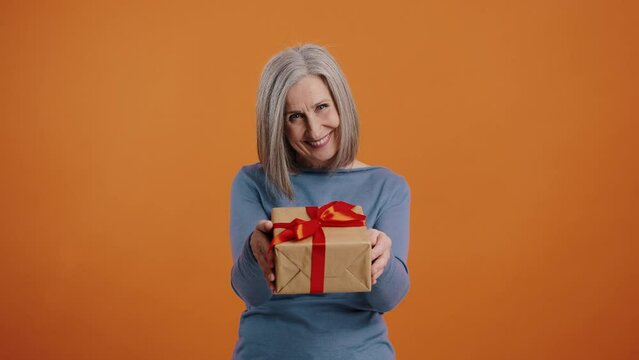 Smiling elderly woman offers gift in package with red bow