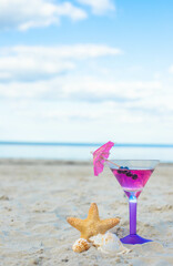 Fototapeta na wymiar Glass of cocktail on sandy beach and starfish next to sea