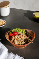 vegan homemade oatmeal in a wooden bowl with fruits on grey table