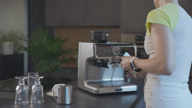 Female is pressing espresso powder down well in the portafilter with tamper. 