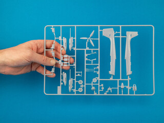 Sprue from a plastic model kit in hand on the blue background. Parts tree of the airplane model....