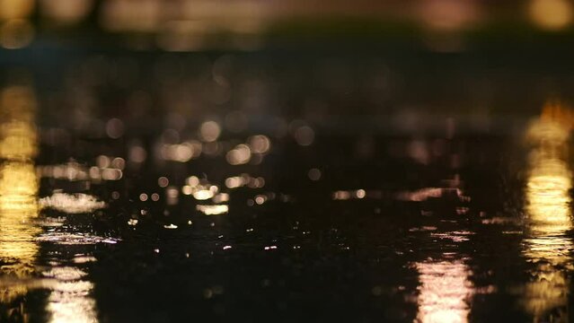 Atmospheric video of rainstorm in a night city. Heavy rain and splashes puddles taken from low point. Large drops break on the pavement in the light of street lamps. Slow motion
