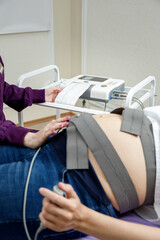 A doctor performs cardiotocography on a young pregnant woman. Selective focus.