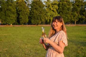 Cute smiling girl holding two bottle of beer at summer park. Positive facial expression, outdoor,...