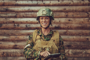 Woman soldier using tablet computer against old wooden wall in camp