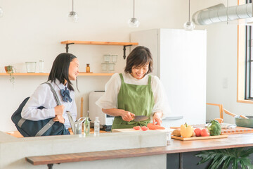 家のキッチンで食事を作るママと娘（小学生・中学生・高校生の女の子）
