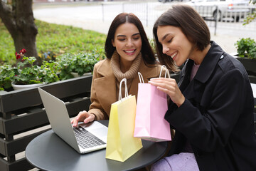 Special Promotion. Happy young women with shopping bags using laptop in outdoor cafe