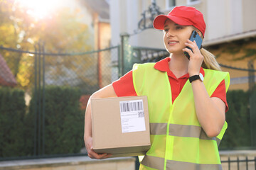 Courier in uniform with parcel talking on smartphone near private house outdoors, space for text