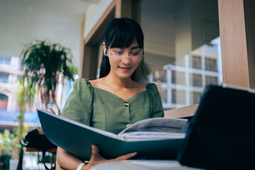 Smiling designer Asian girl  in casual clothing wear glasses using tablet computer connected to...