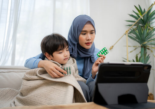 Asian Muslim Mother And Her Sick Son Using A Tablet While Having Video Call With Family Doctor For Advice A Medicine.