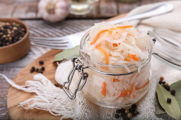 Glass jar of tasty sauerkraut and ingredients on wooden table