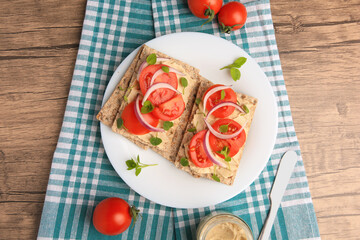 Fresh crunchy crispbreads with pate, tomatoes, red onion and greens on wooden table, flat lay