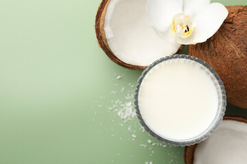 Glass of delicious vegan milk, coconuts and flower on green background, flat lay. Space for text