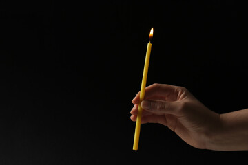 Woman holding burning church candle on black background, closeup