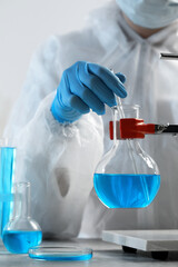 Scientist taking sample of light blue liquid in laboratory, closeup