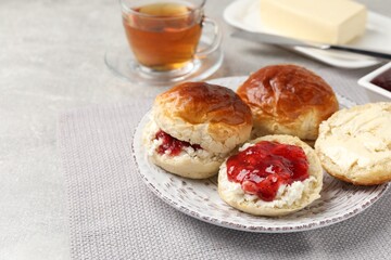 Obraz na płótnie Canvas Freshly baked soda water scones with cranberry jam, butter and cup of tea on light grey mat. Space for text