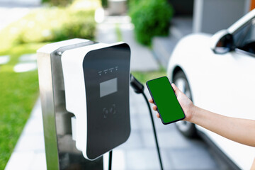 Mockup phone with green screen display energy status of electric vehicle connected to charging station for copyspace. Progressive concept for clean environment. EV powered by green renewable energy. - obrazy, fototapety, plakaty