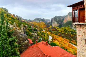 View from the Monastery of St. Barbara or Roussanou at Meteora, Greece under foggy, cloudy skies with leaves turning vibrant fall colors at autumn.	