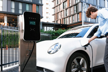 Progressive businessman insert charger plug from charging station to his electric vehicle with...