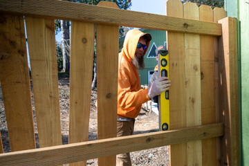 Using a Level Tool to Measure Wood Pickets on Fence For Leveling on Work in Progress