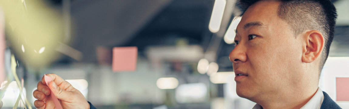 Close up of asian businessman is glues sticky notes on motivation board in modern office