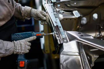 Worker prepares to screw car body parts on workshop conveyor