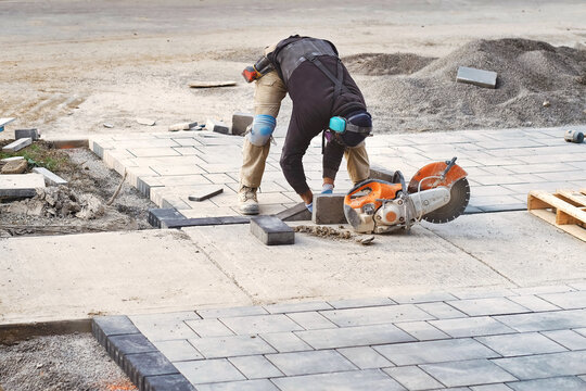 Landscape worker cutting and laying paving stones on residential driveway of a landscaping interlock construction site. Home renovation and improvement work business industry background.