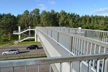 A modern concrete footbridge with guardrail over the freeway. Pedestrian stairs. Side view.