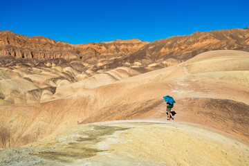 A lone figure with blue umbrella looks at a remote desert landscape.