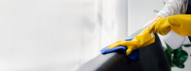 Person cleaning the room, cleaning staff is using cloth and spraying disinfectant to wipe the sofas...